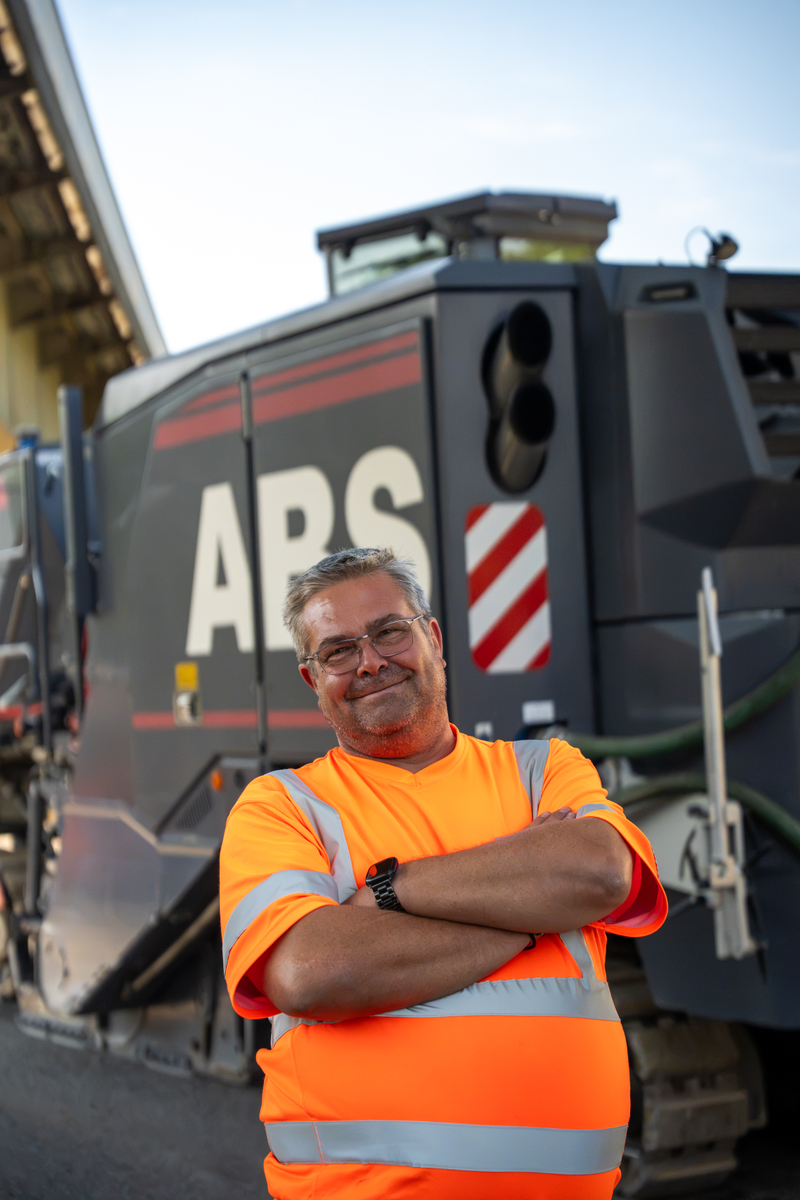 Mitarbeiter von ABS in orangefarbener Warnweste mit verschränkten Armen vor der Fräse