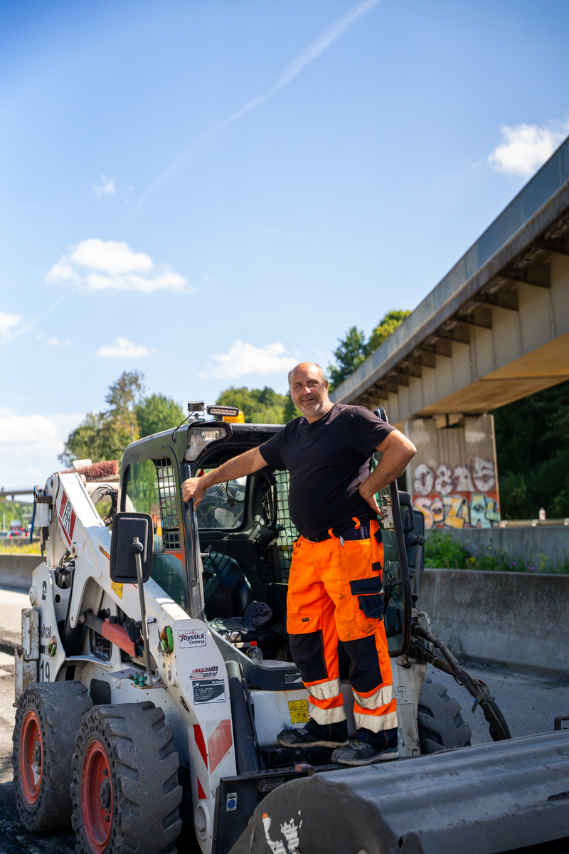Arbeiter von ABS steht auf einem Bobcat unter einer Brücke