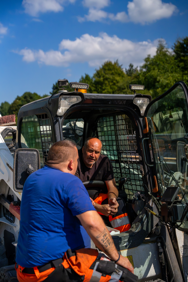 Zwei Arbeiter von ABS sprechen sich an einem Bobcat ab