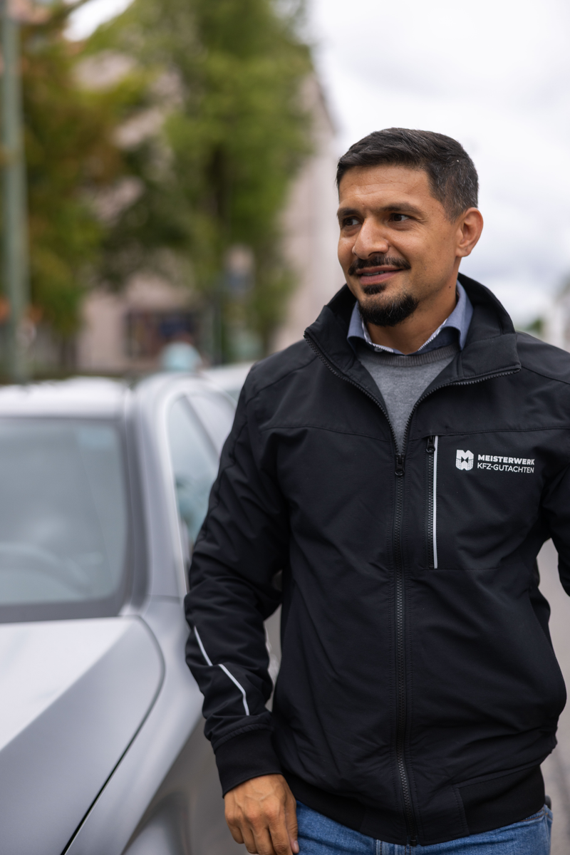 Hamed lächelt in seiner Meisterwerk Jacke neben einem Auto