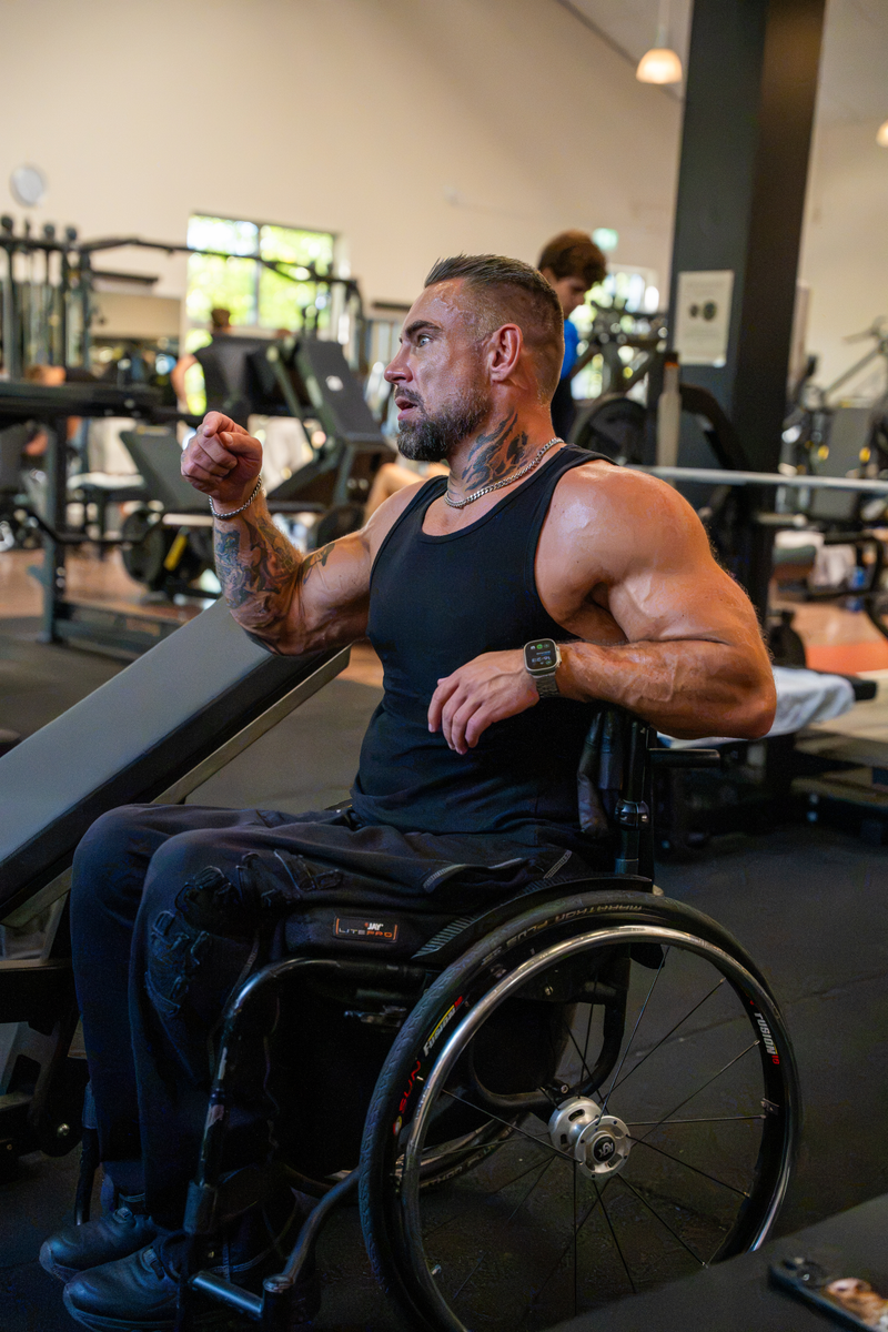 Kim-Andre Brüske spannt im Rollstuhl im Fitnessstudio die Arme an
